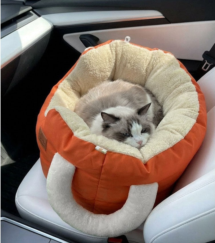 Cat lying in an orange and beige pet bed inside a car.
