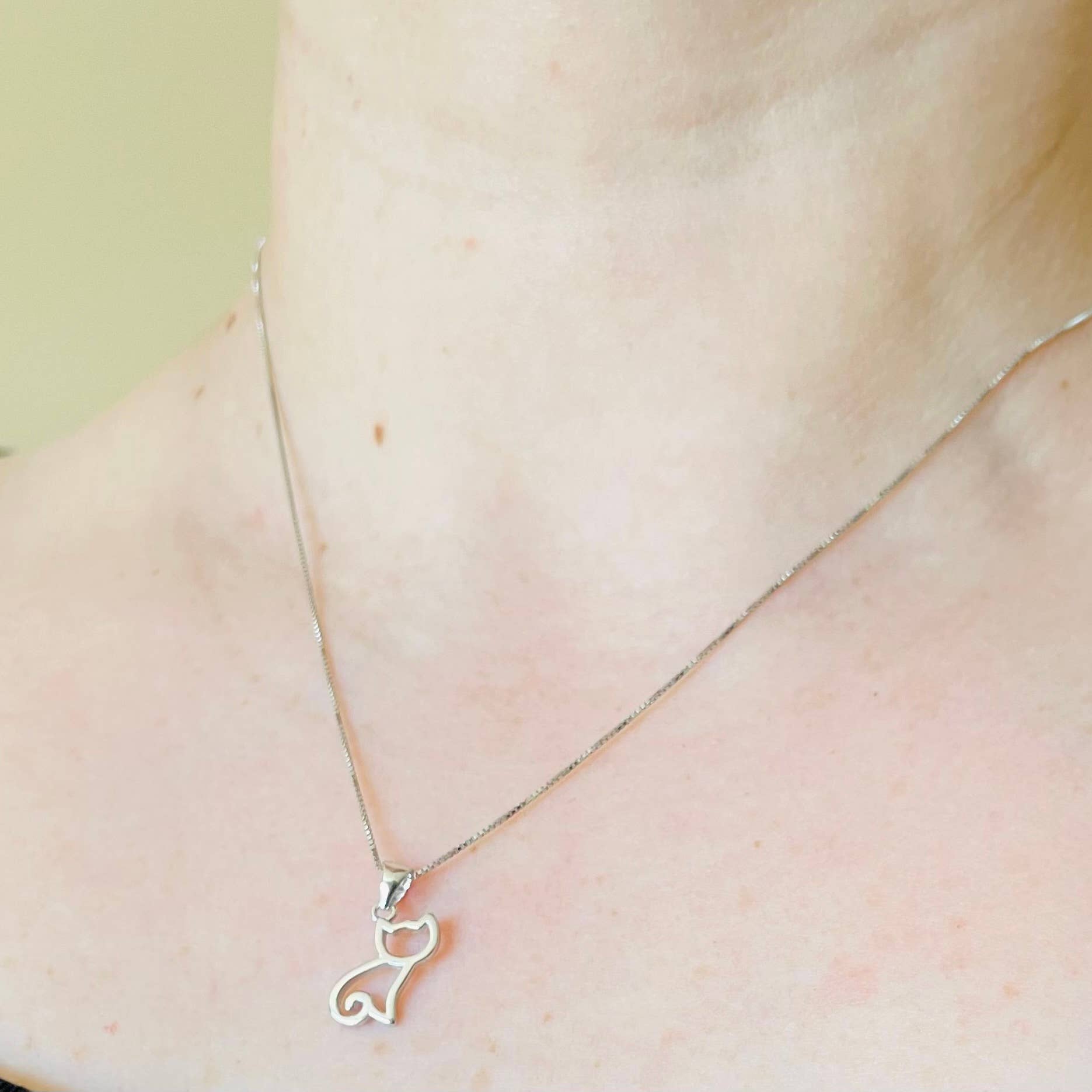 Silver necklace with a cat-shaped pendant on a person's neck against a neutral background