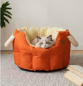 Cat sleeping in an orange pet bed with a beige interior on a carpeted floor.