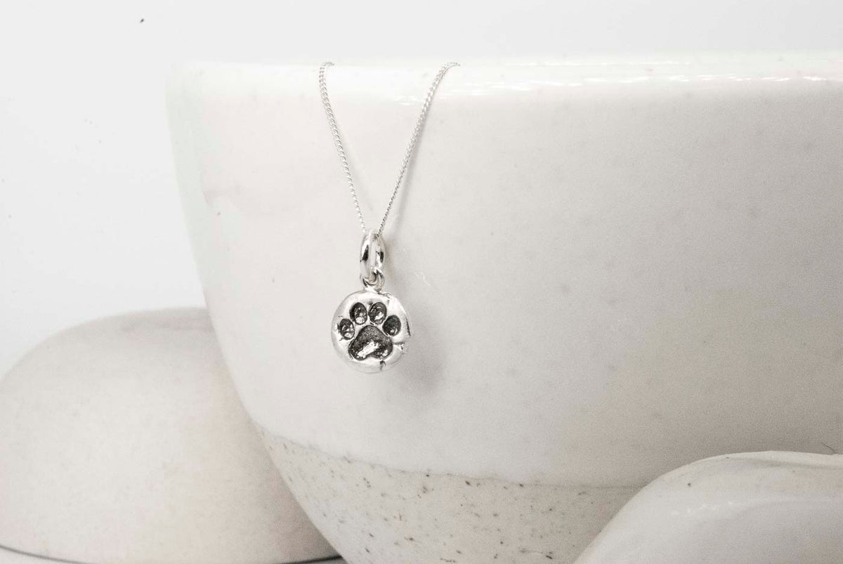 Silver paw print necklace on a white ceramic dish