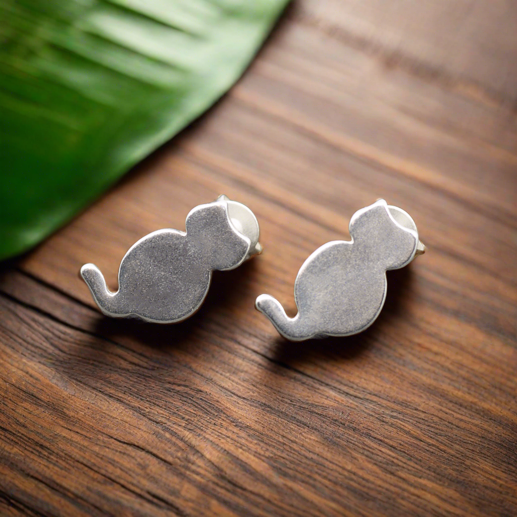 Silver cat stud earrings displayed on wooden surface