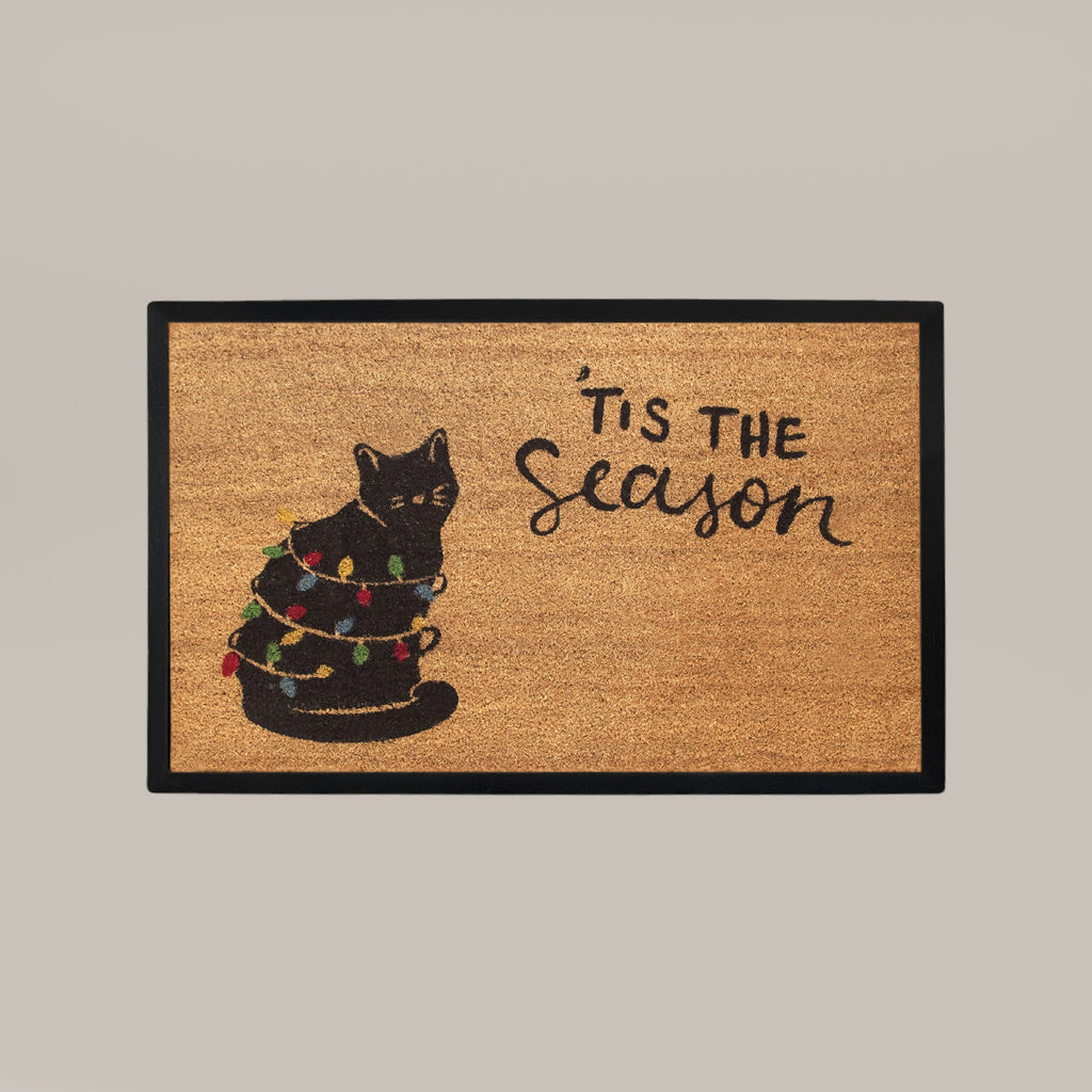 Doormat with a black cat and Christmas lights design and 'Tis the Season text on a beige background.