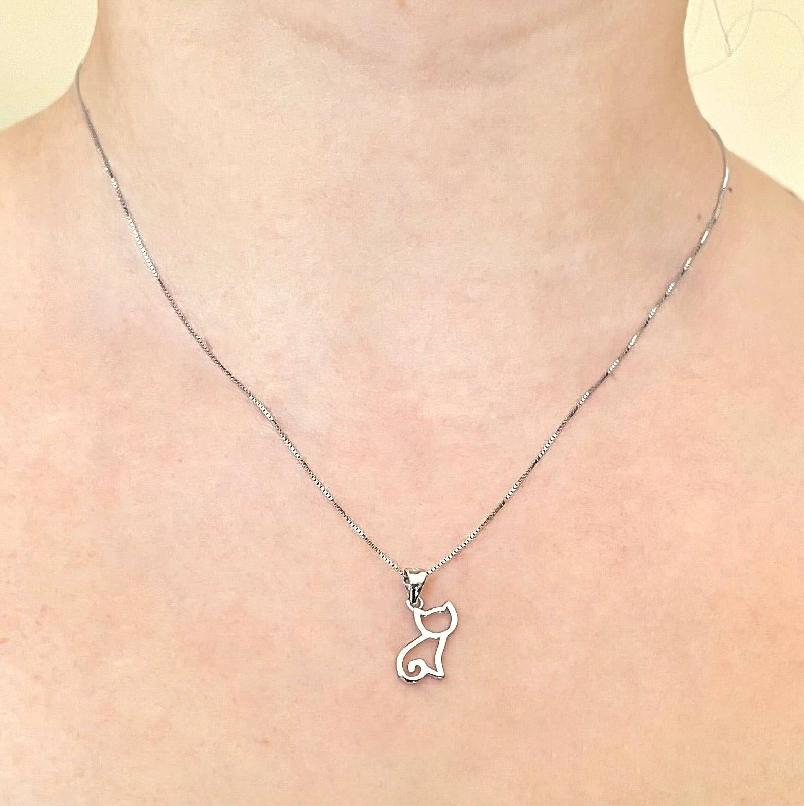 Silver cat pendant necklace on a person's neck against a light background